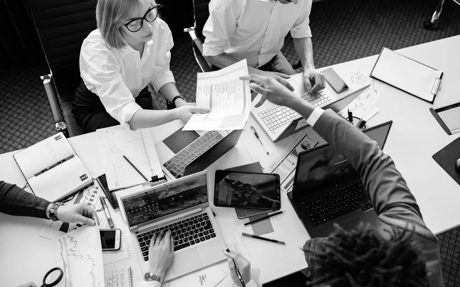 Colleagues working over documents and laptops at a desk, seen from above